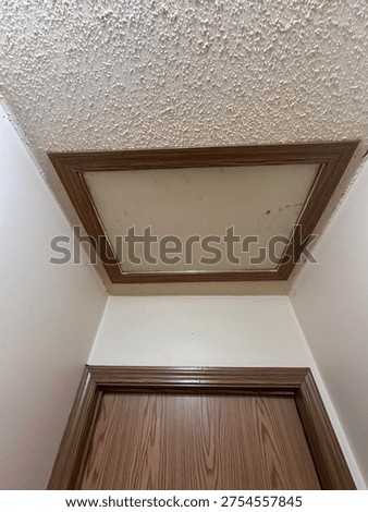 Attic access panel installed in hallway ceiling with wooden trim frame