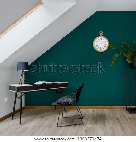 Attic home office room with simple desk and chair and big golden clock on emerald green wall