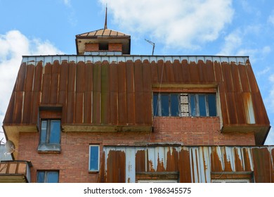 The Attic Of An Old Brick Apartment Building Against The Blue Sky. The Attic Is Finished With Iron Sheets That Have Rusted Over The Years