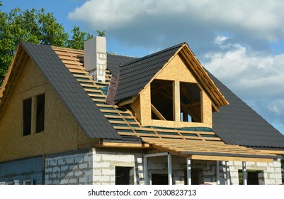Attic roofing construction. A close-up of a wood roof framing over a vapor barrier and metal roof tiles installation, attic windows, chimney construction with insulation.  - Shutterstock ID 2030823713