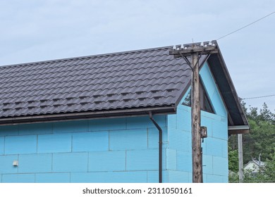 attic of a rural private house with a small window insulated with blue foam under a brown tiled roof on the street against a gray sky - Shutterstock ID 2311050161