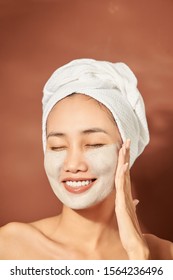 Attracitve young Asian woman applying clay mask on her facee. Spa and wellness, skin care product concept.