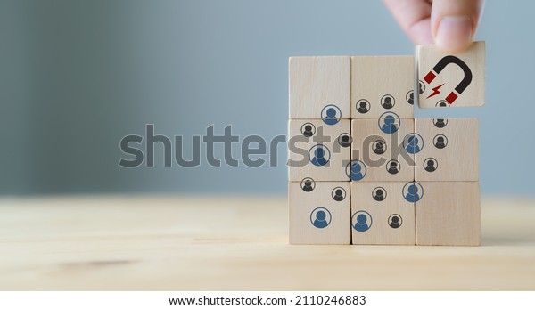 Attracting online customer and lead
generation concept. Digital inbound marketing, customer retention
strategy.Hand hold wooden cube with the icon big magnet to attract
many people on grey
background.