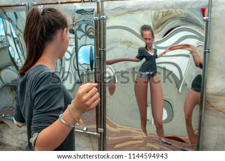 attraction, girl looking at her image in the distorted mirror in the hall of mirrors