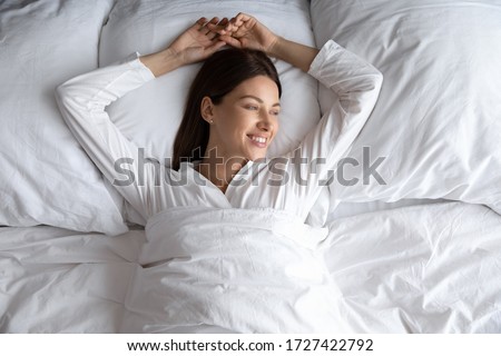 Attractive 30s carefree woman in comfy pyjamas lying down alone in comfortable bed after night enough sleeping woke up feels good top view. Enjoy fresh bedding, new sheet hotel room vacation concept