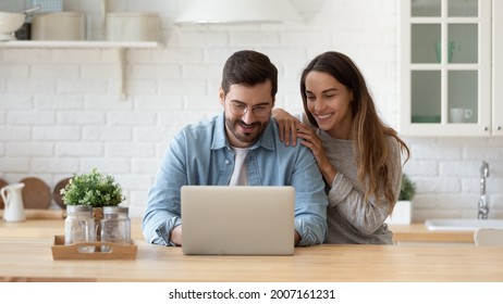 Attractive 35s couple sit at table in cozy kitchen looking at laptop screen, buying goods, tickets online, using e-commerce retail e-services feel satisfied, enjoy comfort usage of modern technology - Powered by Shutterstock