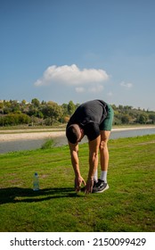 Attractive adn handsome guy is stretching himself before trainnig on the grass, by the river