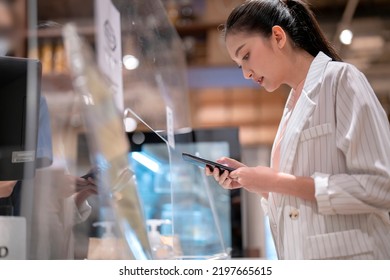 attractive adult asian female cashless online payment smartphone application progress purchase scanning qr code by touchless device new lifestyle shopping in cafe coffee shop store cashier counter
