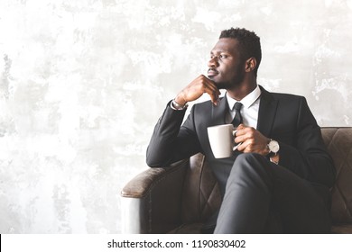 Attractive African American Man In A Business Suit In A Stylish Interior. Businessman And Company Leader. Man Drinks Morning Coffee Before Work For Vivacity