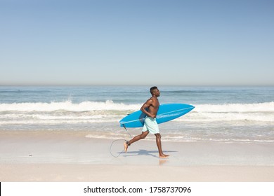 An attractive African American man enjoying free time on beach on a sunny day, smiling, having fun, running with his surfboard, sun shining on him. - Powered by Shutterstock