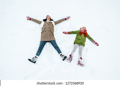 Attractive African American Mother And Cute Daughter Doing Snow Angels In Winter Forest