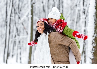 Attractive African American Woman Giving Piggyback Ride To Smiling Daughter In Winter Park