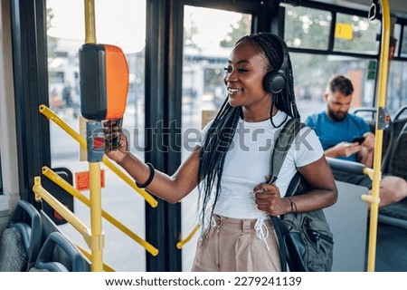 Attractive african american woman paying a bus ticket with her smartphone. Young beautiful woman using public transportation and standing in the bus during a ride. Contactless payment.