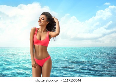 Attractive African American Woman With Perfect Fit Body Relaxing On The Beach, Wearing Pink Fashionable Swimsuit. Sunny Summer Vacation Day.