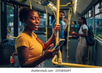 An attractive african american woman using a smartphone while riding a bus in the night. Young beautiful black woman using public transportation. Illuminated by the city light.