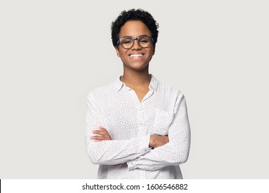 Attractive African ethnicity woman wears casual blouse and glasses pose isolated on gray background standing with arms crossed having wide beautiful smile looks at camera feels confident and healthy