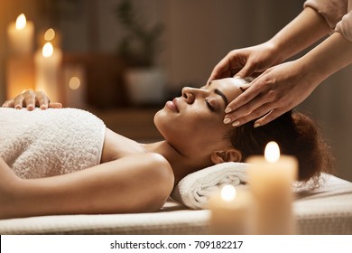 Attractive african girl enjoying face massage in spa salon.
