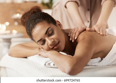 Attractive african girl having massage relaxing in spa salon. Closed eyes.