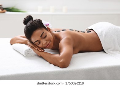 Attractive african girl lying at spa salon, getting hot stone massage, healhcare concept