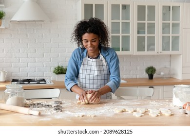 Attractive African housewife prepare pastries, kneading dough cooking alone standing in modern cozy domestic kitchen, making homemade biscuits recipe enjoy process and cookery, routine, hobby concept - Shutterstock ID 2089628125