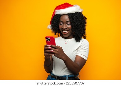 Attractive african lady in Santa hat using her cellphone on yellow background - Powered by Shutterstock