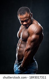 Attractive african male fighter or boxer posing shirtless, isolated over dark background. Toned and ripped muscle fitness man under dramatic low key lighting.