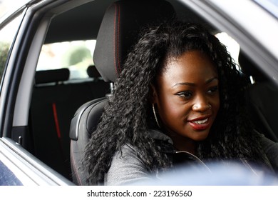 Attractive African woman with long curly hair seated in a motor car viewed through the open side window