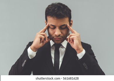 Attractive Afro American businessman in classic suit is touching his temples while concentrating, on gray background - Shutterstock ID 561681628