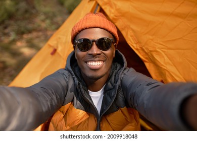 Attractive afro american guy taking selfie to remember. Using modern technology in wild nature. Orange tent on background. Lust for life, seek for adventure, travelling alone concept