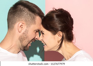 The attractive angry couple fighting and shouting at each other. quarrel concept. The studio shot on trendy pink and blue background. Human emotions concept