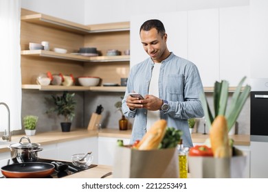 Attractive Arab Man Preparing Romantic Dinner On Home Kitchen. Serious Concentrated Guy Looking For Good Recipe At Smart Phone. Healthy Food Menu App. Cookbook Mobile Application. Technology And Home