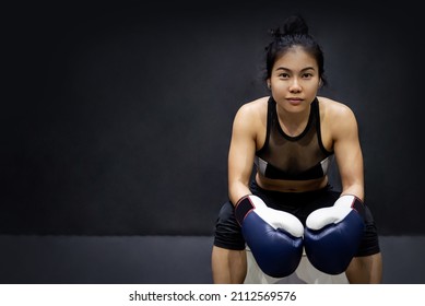 Attractive Asian Boxer Woman Sitting And Posing With Blue Boxing Gloves In Fitness Gym. Female Boxing Class And Martial Art Concept