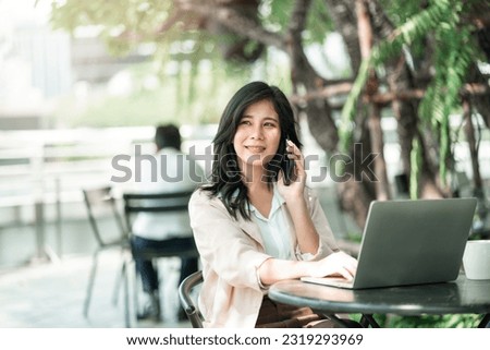 Attractive asian business woman using smartphone for talking with colleague while using laptop for work at co-working space, Urban business people, work anywhere lifestyles.