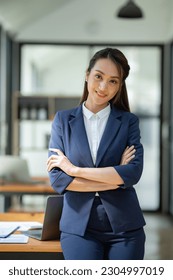 Attractive asian businesswoman standing with crossed arms and looking at camera in office confident and happy with business success - Shutterstock ID 2304997019