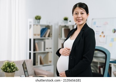 Attractive asian chinese pregnant woman in suit working in light modern office. confident maternity future mom employee standing in workplace face camera smiling indoors. happy motherhood worker. - Powered by Shutterstock