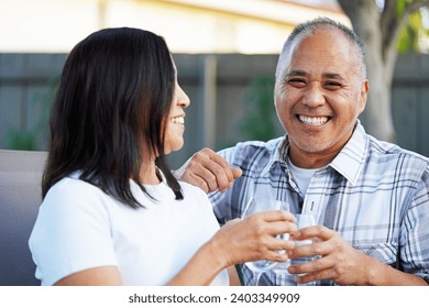 Attractive Asian couple sits outside in the garden in the afternoon holding wine glasses and making a toast while smiling - Powered by Shutterstock