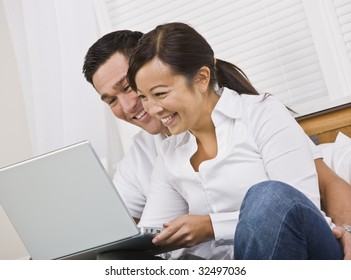 Attractive Asian Couple Smiling While Looking At A Laptop Screen Together. Horizontally Framed Photo.