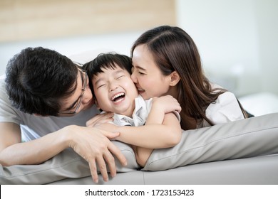 Attractive Asian Family Happy And Smile, Little Boy Received Kiss And Hug From Father And Mother Sitting On Sofa At Home