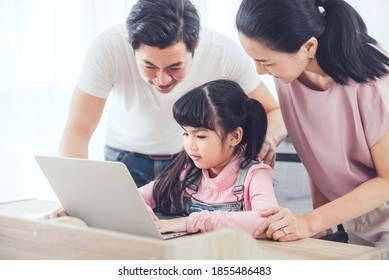 Attractive Asian Family (mother, Father, Child Daughter) Smiling And Using Laptop Computer Together While Sitting At Table In Home.