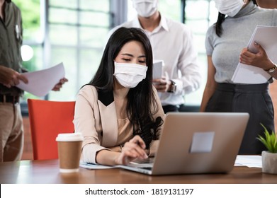 Attractive Asian Female Boss Supervisor Wear Protective Face Mask In New Normal Office Teaching And Explaining Intern Or New Employee To Use Corporate Software Or Helping With Difficult Assignment