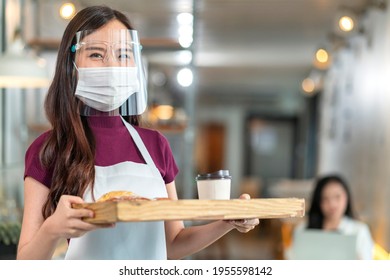 Attractive Asian Female Cafe Worker Wears Face Mask And Gloves Giving Takeaway Food Bag To Customer. 
Waitress Holding Takeout Order Standing In Coffee Shop Front Door Entrance New Normal Lifestyle