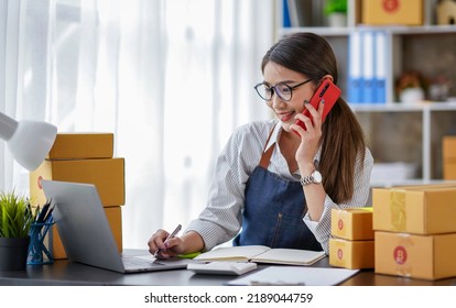 Attractive Asian Female Entrepreneur Woman Work With A Smartphone, Young Asian Small Business Owner Use Computer, Online Market Packing Box Delivery, SME E-commerce Telemarketing Concept