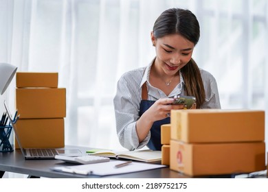 Attractive Asian Female Entrepreneur Woman Work With A Smartphone, Young Asian Small Business Owner Use Computer, Online Market Packing Box Delivery, SME E-commerce Telemarketing Concept