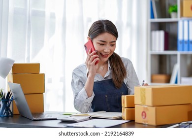 Attractive Asian Female Entrepreneur Woman Work With A Smartphone, Young Asian Small Business Owner Use Computer, Online Market Packing Box Delivery, SME E-commerce Telemarketing Concept