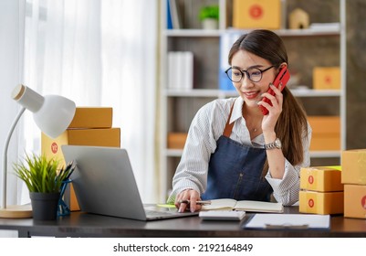 Attractive Asian Female Entrepreneur Woman Work With A Smartphone, Young Asian Small Business Owner Use Computer, Online Market Packing Box Delivery, SME E-commerce Telemarketing Concept