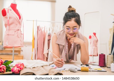 Attractive Asian Female Fashion Designer Working In Home Office Workshop. Stylish Fashionista Woman Creating New Cloth Design Collection. Tailor And Sewing. People Lifestyle And Occupation Concept