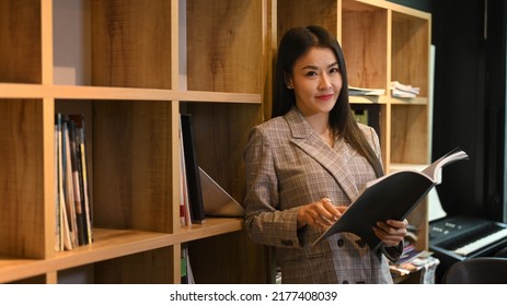 Attractive Asian Female Manger Standing Near Bookshelves In Bright Company Office