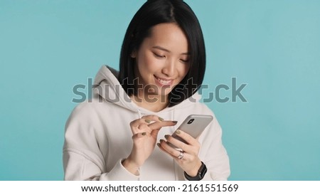 Attractive Asian girl choosing photos for social network using smartphone over blue background