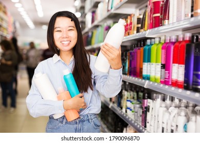 Attractive Asian Girl Holding Plastic Bottles Of Shampoo And Hair Balms In Cosmetics Store