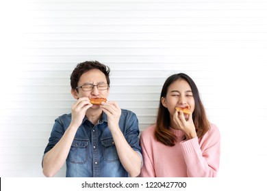 Attractive Asian Hungry Couple Eating Pizza Or Fast Food With Smile And Tasty Facial Expression On Face With White Wall Background. Millennial Lifestyle With Friends Concept. Man And Woman Enjoy Meal.